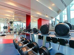 Ein Fitnessraum mit Gewichten, darunter Kurzhanteln und Langhanteln, sowie eine Spiegelwand.