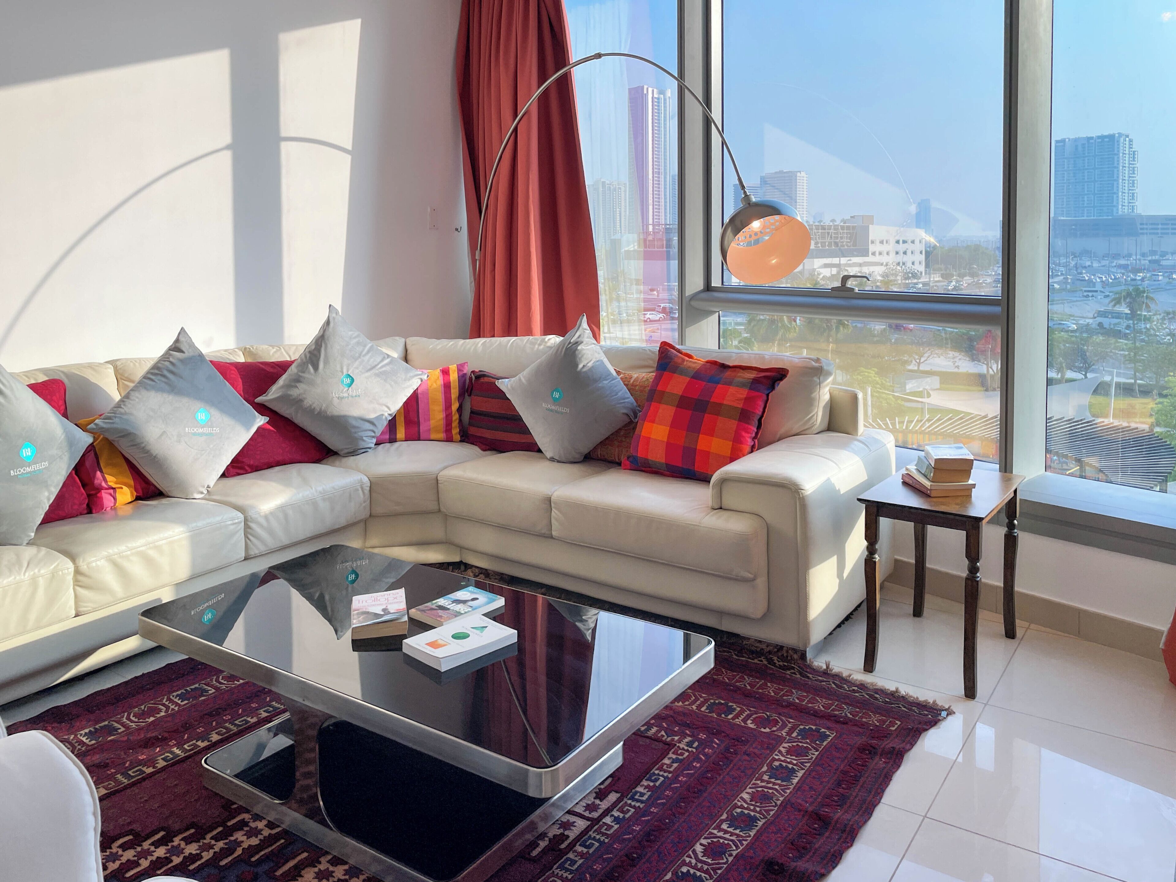 A modern living room with a sofa, coffee table, and a view of the cityscape through large windows.