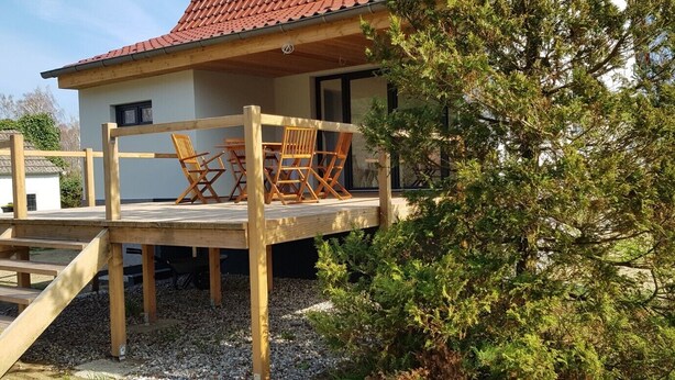 Eine Holzterrasse mit Gartenmöbeln, einer Treppe und einem Haus mit rotem Dach.