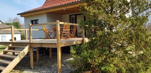 Puisesta laudasta rakennettu terassi, jossa on ulkokalusteita, portaikko ja punaisella katolla varustettu talo.