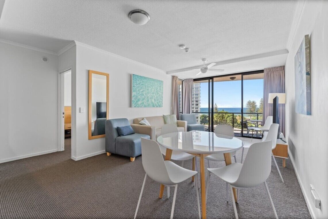 A modern hotel room with a balcony, a round dining table, and a sofa.