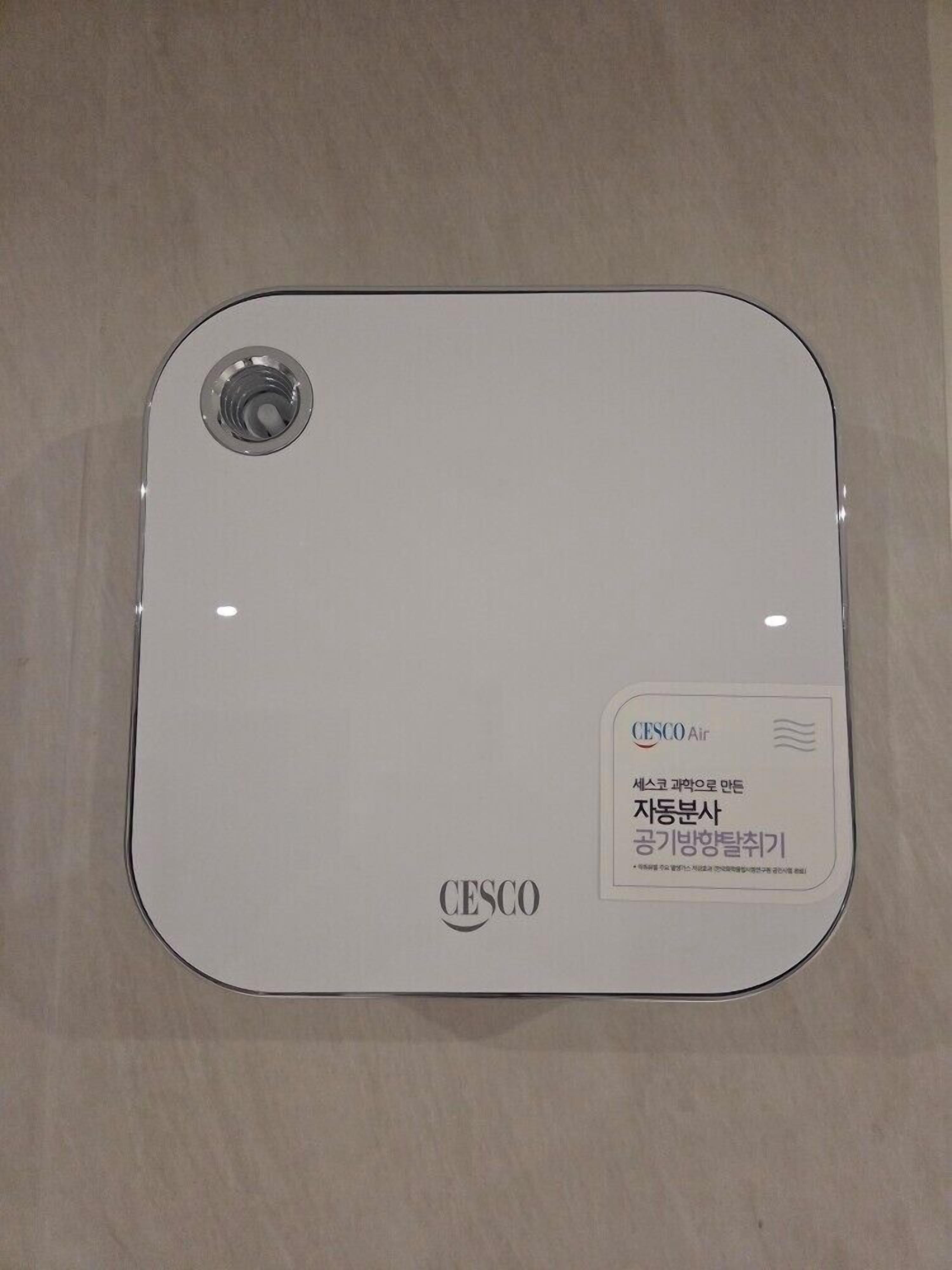 Un objeto blanco y cuadrado, con un detalle circular en un lado y etiquetas de texto que incluyen 'CESCO' y 'CESCO Air' en el otro.