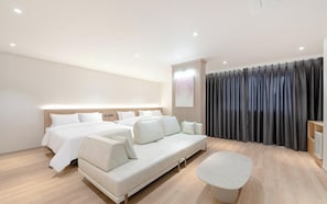 Una habitación de hotel moderna con una cama grande, un sofá, una mesita y una cortina.