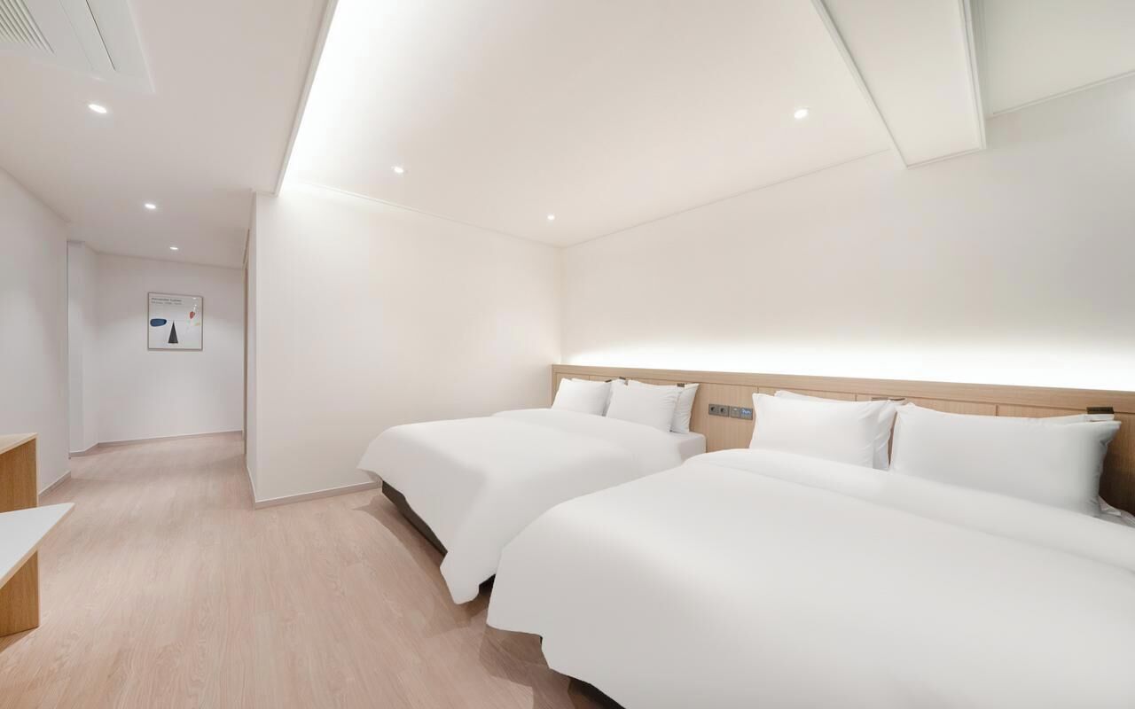 Habitación de hotel con dos camas, un cabecero de madera, una pared blanca y suelo de madera.