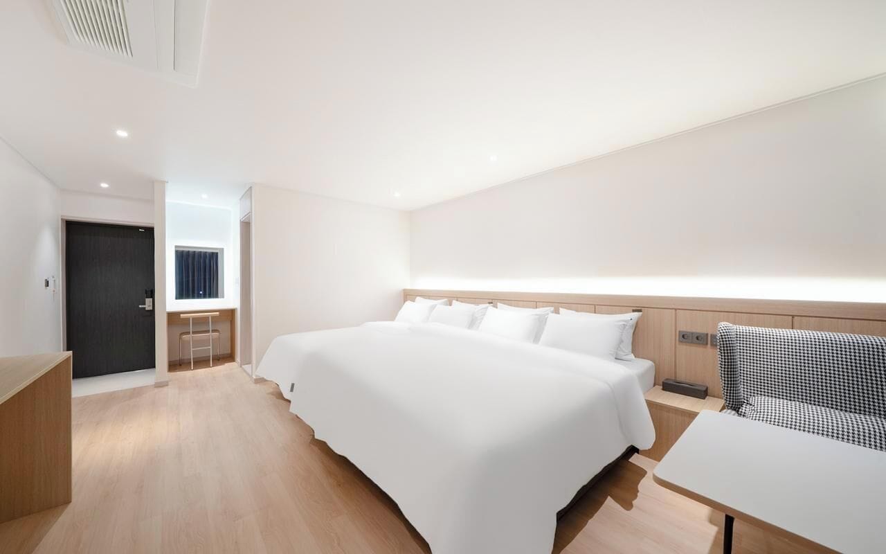 Una habitación de hotel moderna con una cama grande, una mesita de noche, un sofá y vistas a la ciudad.