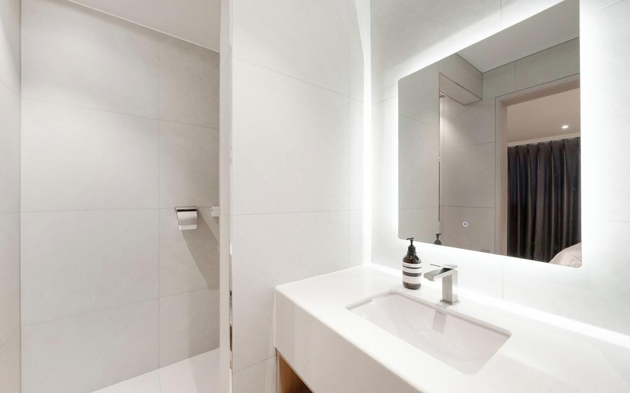 Uma casa de banho moderna com uma pia branca, um espelho e uma área de duche.
