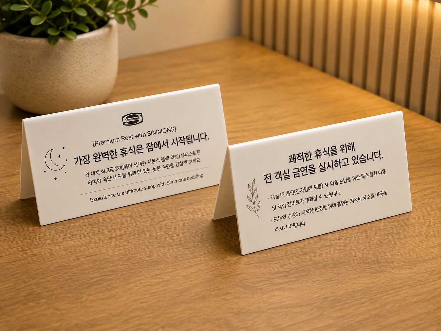 Two white business cards on a wooden table with a potted plant in the background.