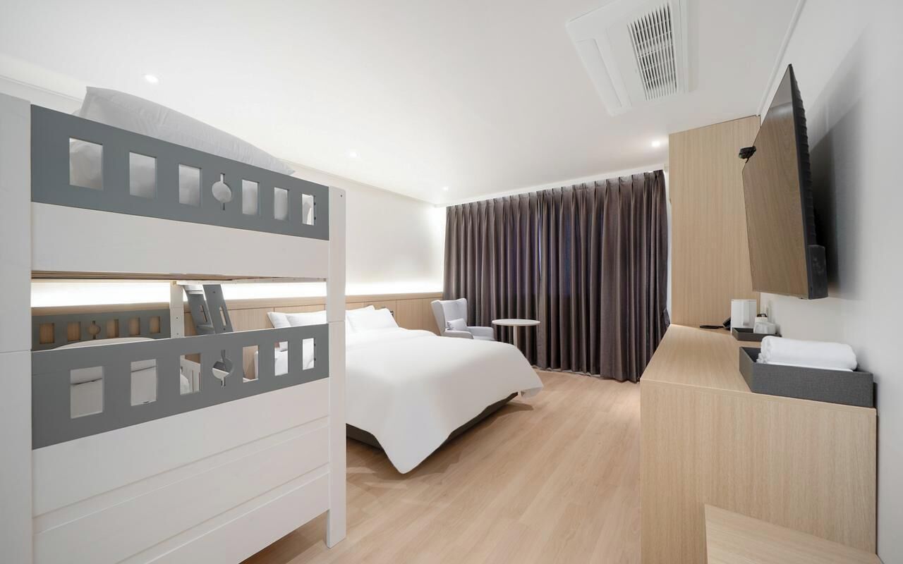 Een moderne hotelkamer met een stapelbed, een bureau, een stoel, een flatscreen televisie en een groot raam met gordijnen.