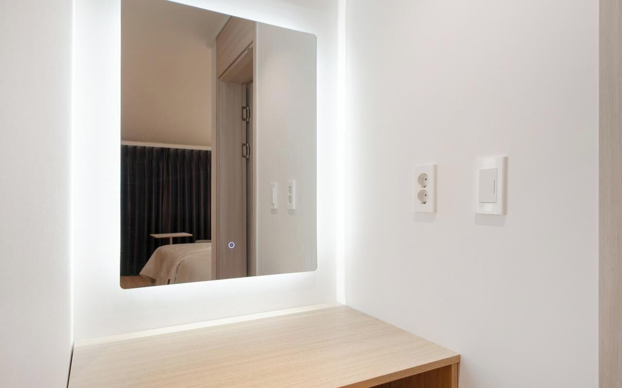 Un baño con un espejo, un interruptor de luz y una toma de corriente en la pared.