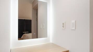 Un baño con un espejo, un interruptor de luz y una toma de corriente en la pared.