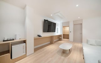 Habitación de hotel moderna con televisión de pantalla plana, sofá blanco, mesa de centro y minibar.