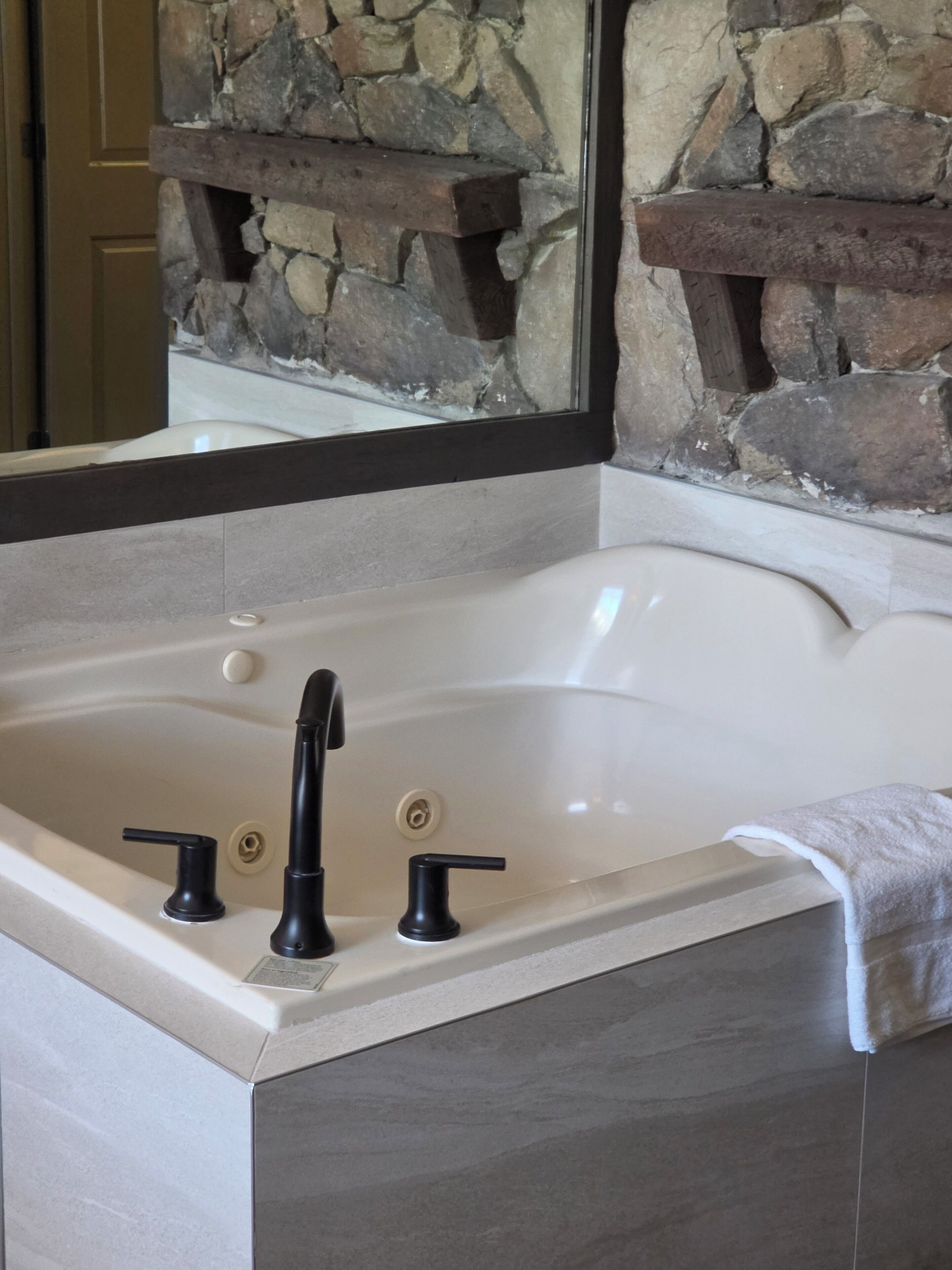 A modern bathroom with a stone wall, a large bathtub, and a mirror.