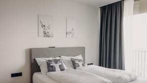 A neatly made bed with white linens and a grey headboard, accompanied by decorative pillows. - Panorama Apartment Monte Central (Neukirchen am Grossvenediger)