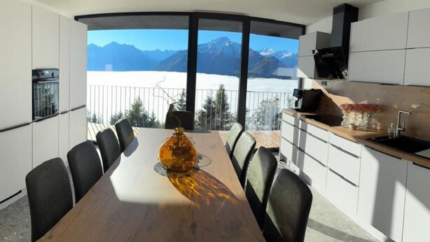 A modern kitchen with a dining area, large windows, and a view of mountains. - Panorama Apartment Monte Central (Neukirchen am Grossvenediger)
