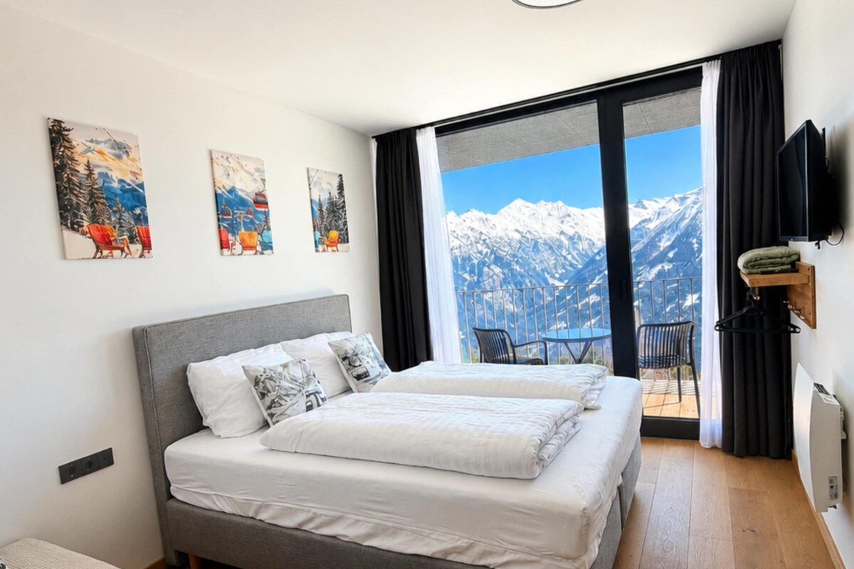 Quarto com uma cama grande, varanda com vista para as montanhas e obras de arte nas paredes.