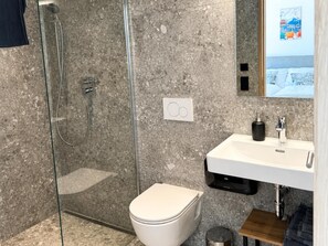 A bathroom with a glass shower enclosure, a white toilet, a sink with a black soap dispenser, and a mirror. - Panorama Apartment Monte Central (Neukirchen am Grossvenediger)