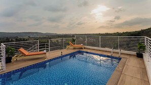 Una piscina en la azotea con dos sillones de descanso, una mesa pequeña junto a la piscina y vistas a colinas distantes.