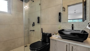 Un baño moderno con cabina de ducha de vidrio, inodoro negro, tocador con lavabo de diseño negro y espejo sobre el lavabo.