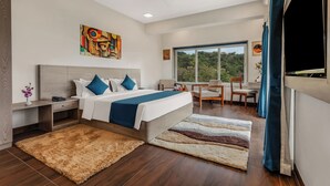 Habitación de hotel moderna con una cama grande, un escritorio, una silla, una ventana con vistas y una obra de arte en la pared.