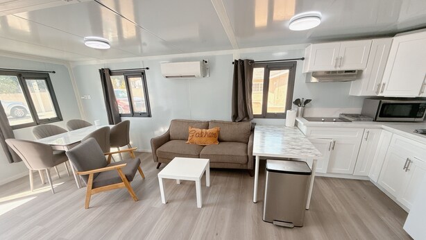 Un salon moderne comprenant un canapé, une table à manger, des chaises, une petite table blanche et un coin cuisine avec des placards et un four à micro-ondes.