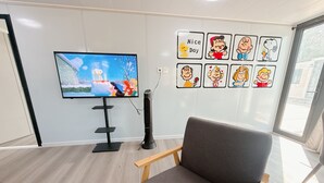 Une pièce avec une télévision, un mur décoré de personnages de dessins animés, une chaise et une fenêtre.