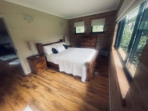 A bedroom with a wooden bed, nightstands, a dresser, and a window with a view of greenery.