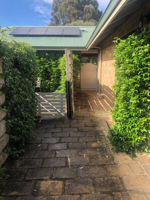 A brick pathway leading to a gated entrance with a green roof and a brick wall.