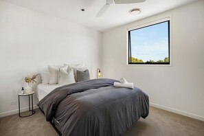 Een slaapkamer met een bed, nachtkastje, lamp en een raam met uitzicht.