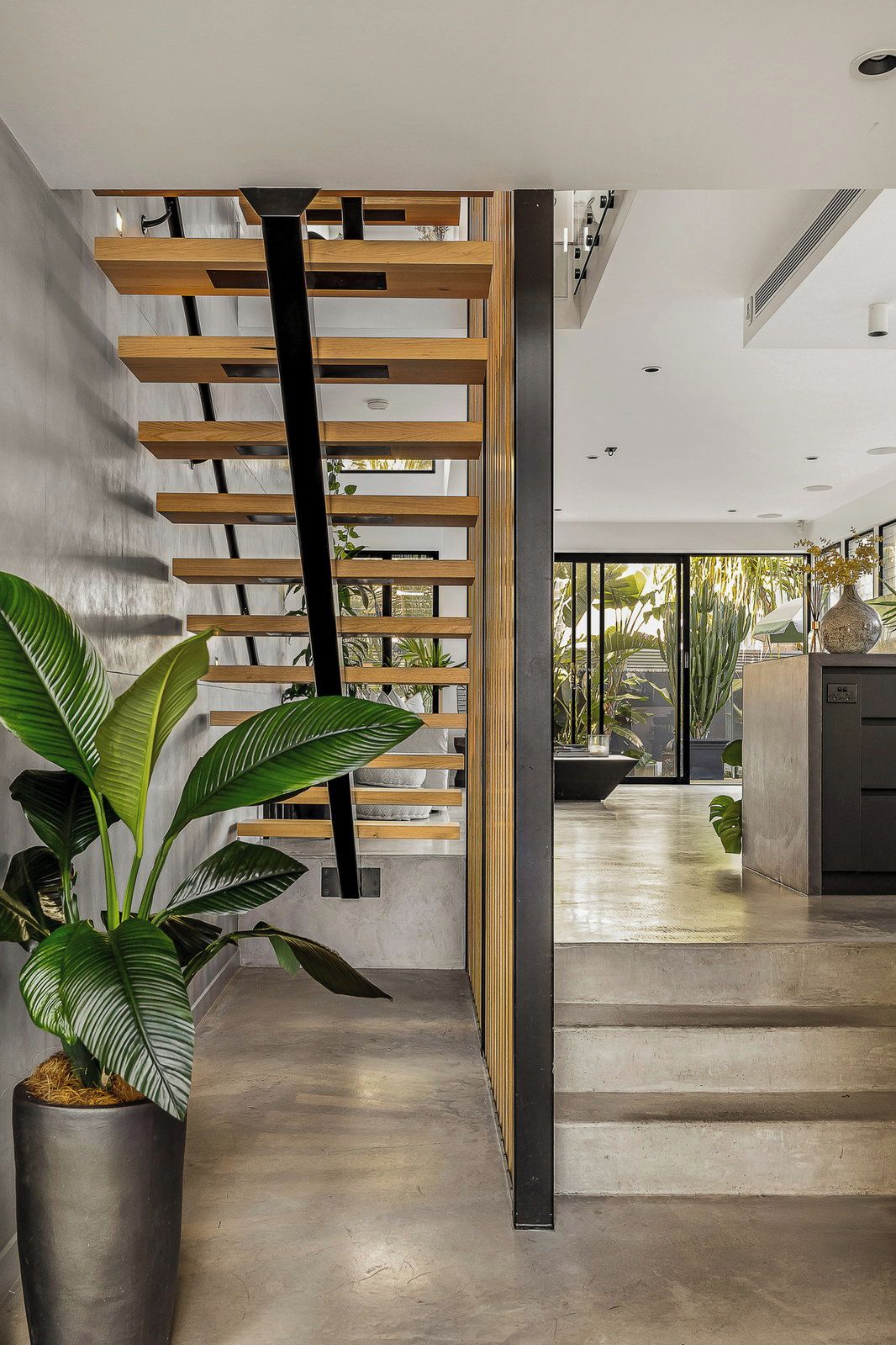 A modern interior with a concrete staircase, a potted plant, and a view of the outdoors.