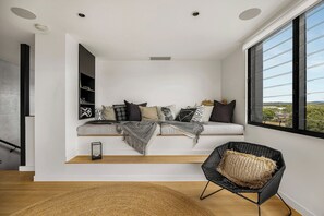 A modern interior with a built-in bench, a black wicker chair, and a view through a large window. - Luxury Villas Urban Tropic (Gold Coast)