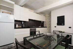 Et moderne køkken med hvide skabe, en sort bordplade og et glas spisebord.