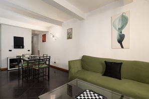 A living room with a green sofa, a glass coffee table, a dining area with a table and chairs, and artwork on the walls. - San Frediano Nest Apartment (Florence)