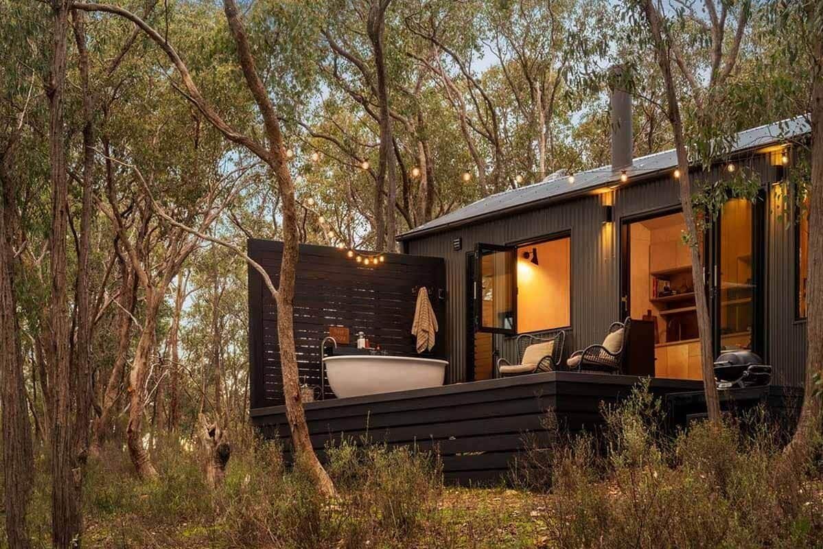 A cabin with a large bathtub, outdoor seating, and a deck overlooking a forest.