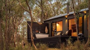 A cabin with a large bathtub, outdoor seating, and a deck overlooking a forest.