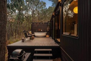 A wooden deck with a hot tub, seating, and a grill.