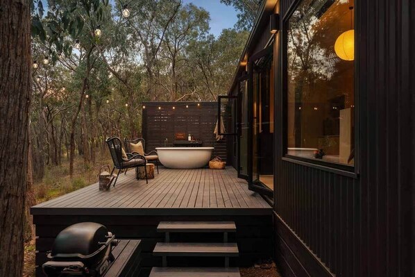 A wooden deck with a hot tub, seating, and a grill.