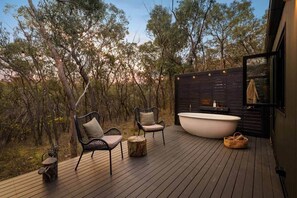 Une terrasse avec deux chaises, une grande baignoire et une table en bois.