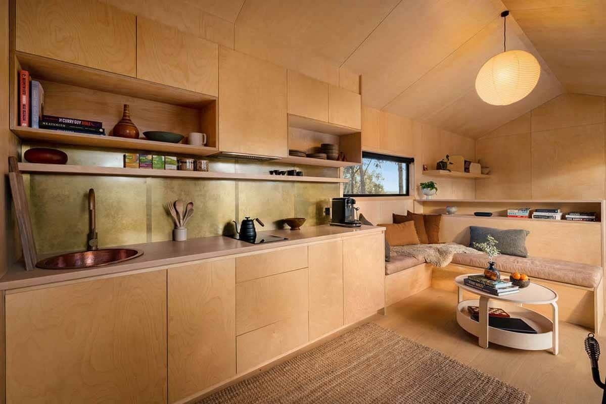 Een moderne keuken met houten kastjes, een koperen spoelbak en een ingebouwde kookplaat. Er is een zithoek met een bank en een salontafel.