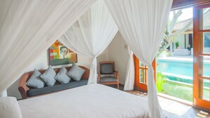 A bedroom with a bed, a chair, a sofa, and a view of a swimming pool. - Villa Sara (Badung)
