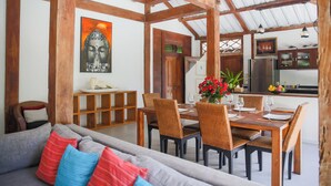 A dining area with a wooden table and chairs, a sofa with cushions, and a painting on the wall. - Villa Sara (Badung)