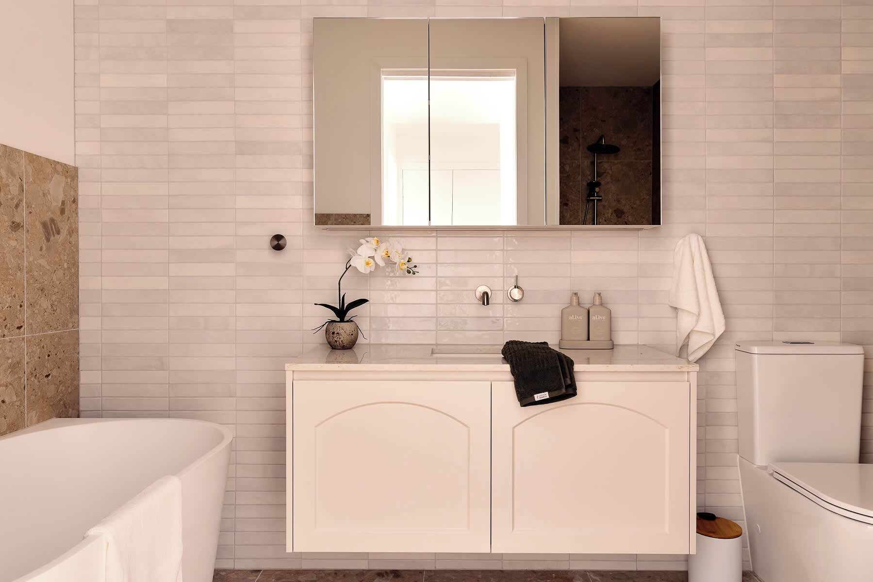 Een badkamer met een wit wastafelmeubel, een spiegel, een wastafel, een toilet en een bad.