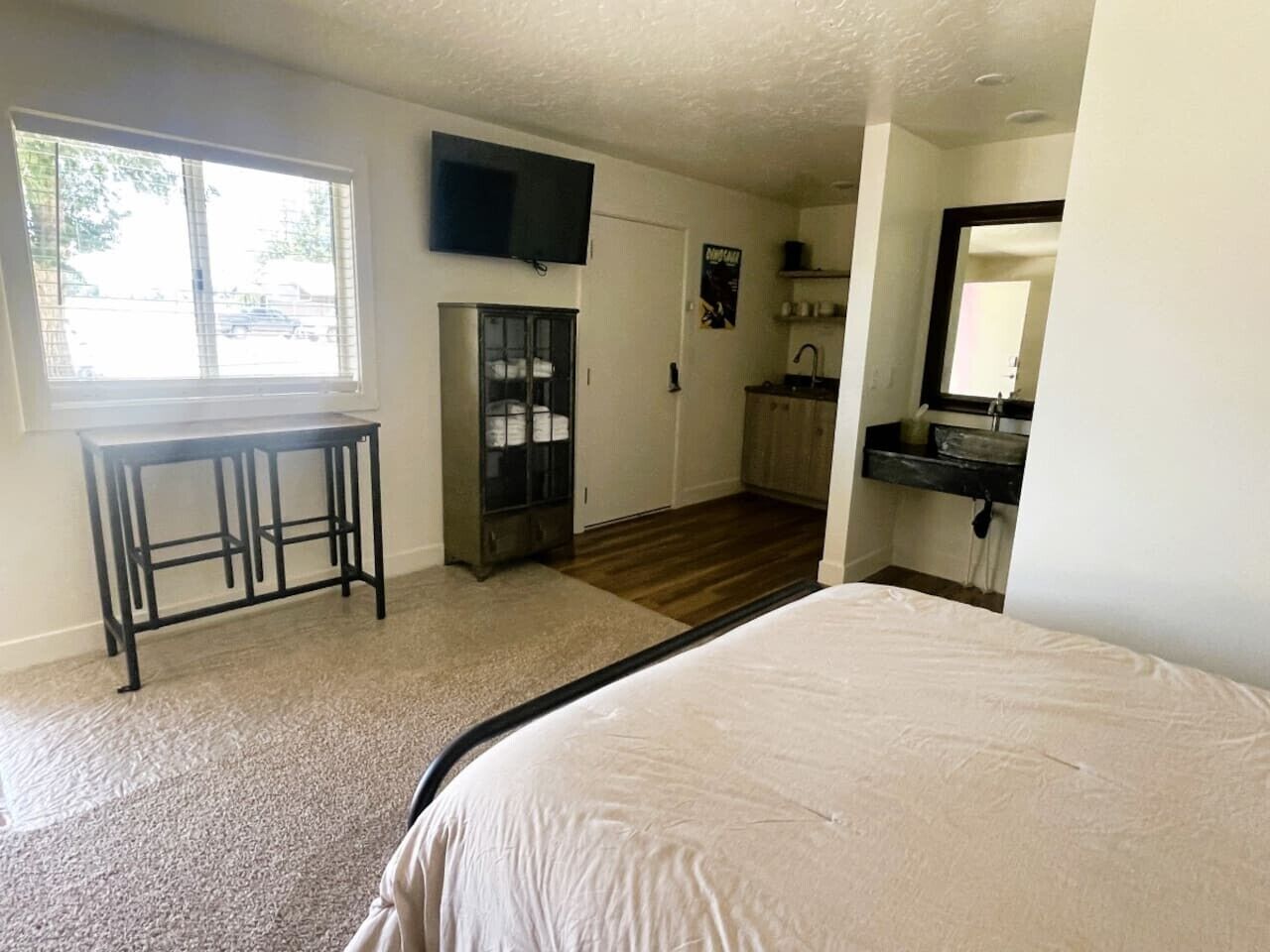 A bedroom with a bed, a desk, a TV, and a view of the outside.