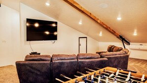 A cozy room with a sofa, a foosball table, and a TV mounted on the wall.