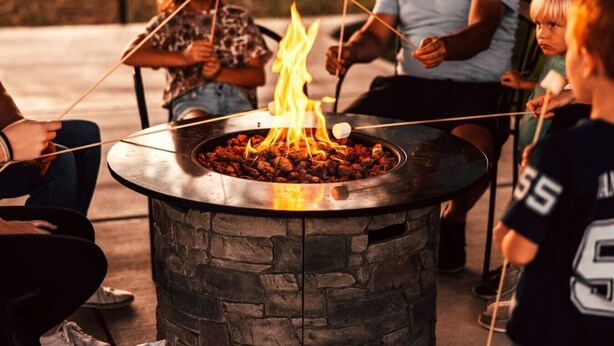 A stone fire pit with flames, surrounded by people.
