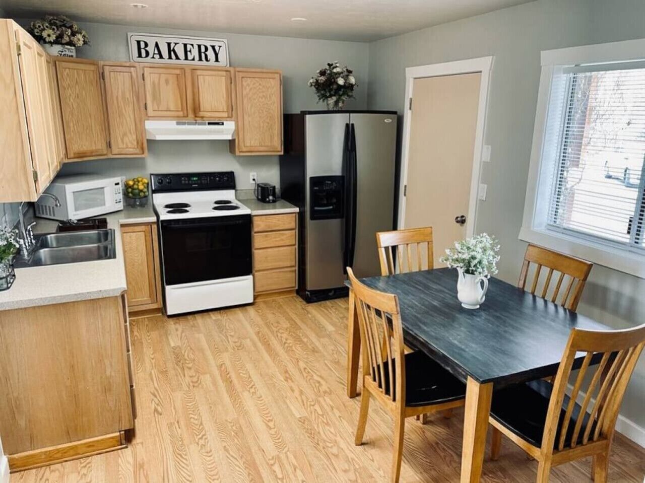 Una cocina con armarios de madera, estufa, refrigerador y una mesa de comedor con sillas.