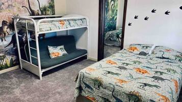Ein Zimmer mit Etagenbett, einem Bett mit Bettwäsche im Dinosaurer-Design, einem Wandbild mit Dinosauriern und einem Spiegel mit einer Naturdarstellung.