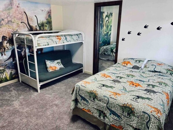 A room with a bunk bed, a bed with a dinosaur-themed bedspread, a mural with dinosaurs, and a mirror with a nature scene.