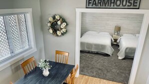 A dining area with a dark wooden table and chairs, a vase with flowers, and a 'FARMHOUSE' sign above a bed. - Dino Trails Getaway South - Sleeps up to 42 People (Jensen)