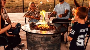 A group of people around a stone fire pit with skewers of food. - Dino Trails Getaway South - Sleeps up to 42 People (Jensen)