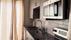 A modern kitchen with stainless steel appliances, a black countertop, and light-colored cabinetry. - Cozy Studio Apt 1.5 Miles to Mercedes Benz Stadium (Atlanta)